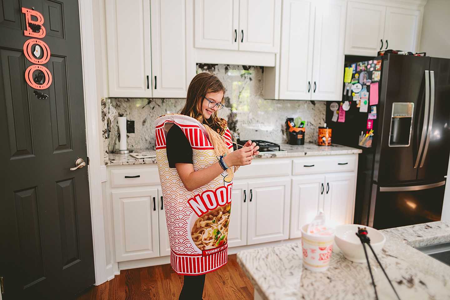 Girl in Noodles Halloween costume laughing in kitchen as she prepares noodle soup
