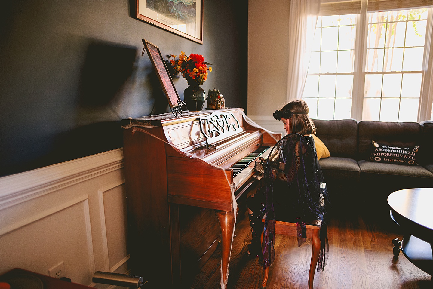 Girl in a dark fairy costume with black wings plays piano in a parlour