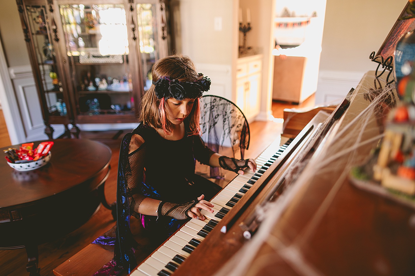 Girl in a dark fairy costume with black wings plays piano in a parlour